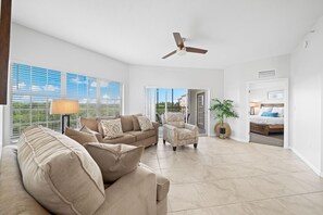 A spacious living room with a ceiling fan, a sofa set, a chair, and a view through a glass door to the outside. - 6406 Spacious 2/2 Resort Condo Near Disney (Orlando)