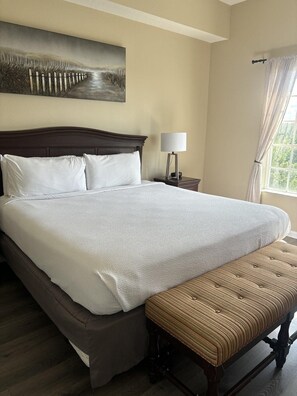 A hotel room with a large bed, a nightstand, a lamp, a window with curtains, and a painting on the wall. - 6503 Spacious 2/2 Resort Condo Near Disney (Orlando)