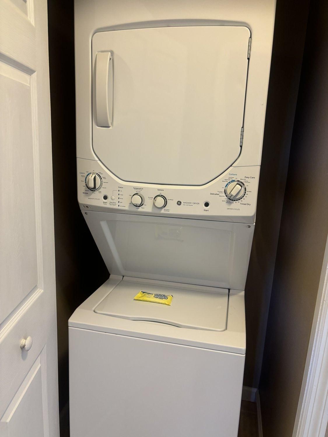 A front-loading washing machine with control knobs and a detergent packet on the door.
