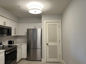A compact kitchen with white cabinets, a stainless steel refrigerator, a microwave, and an oven. - 7107 Luxurious 3/2 Resort Condo Near Disney (Orlando)