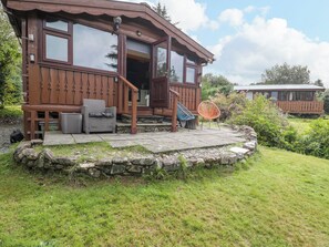 A wooden cabin with a stone foundation, a porch with seating, and a clear sky. - Babbling Brook (Blaenau Ffestiniog)