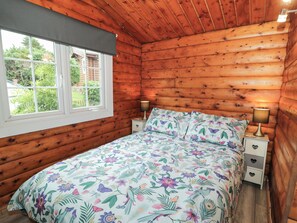 A wooden cabin bedroom with a bed, two bedside tables, and a window. - Babbling Brook (Blaenau Ffestiniog)