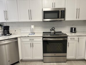 A modern kitchen with white cabinets, a stainless steel microwave, a kettle, and a coffee maker.