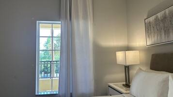 Une chambre d’hôtel avec un lit, une table de chevet avec une lampe, une fenêtre avec des rideaux et un tableau au mur.