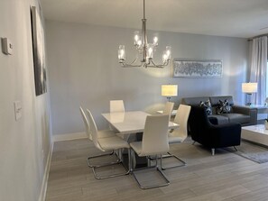 A modern dining area with a white table and chairs, a black sofa, and a chandelier.