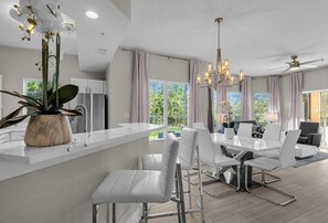 A modern kitchen with a white countertop, a dining area with white chairs, and a chandelier. - 7507 Luxurious 3/2 Resort Condo Near Disney (Orlando)