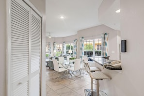 A hotel room with a dining area, a desk with a telephone, and a window with curtains. - 1101 Spacious 3/2 Resort Condo Near Disney (Orlando)