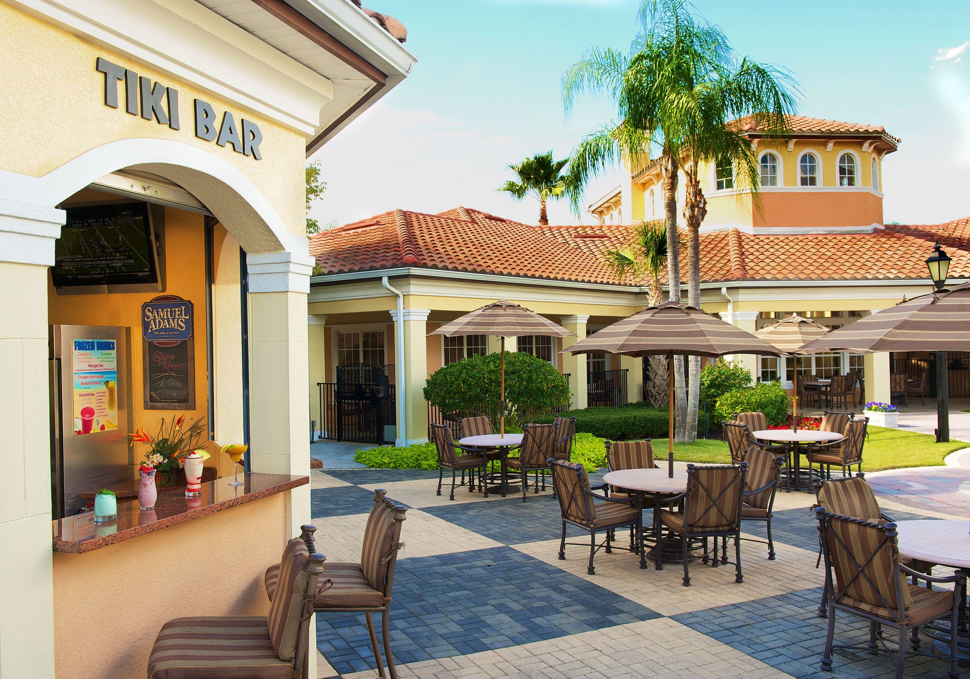 An outdoor seating area with tables and chairs, a bar, and a building with a tiled roof.