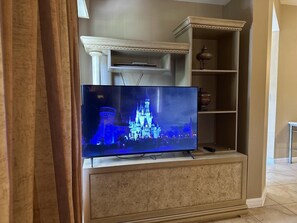 A flat-screen TV mounted on a beige cabinet with a decorative shelf above it. - 1207 Spacious 3/2 Resort Condo Near Disney (Orlando)