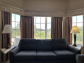 Ein Zimmer mit einem dunkelgrauen Sofa, zwei Lampen und großen Fenstern mit Vorhängen.