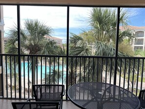 A balcony with a view of a swimming pool, palm trees, and a building in the background. - 1302 Spacious 3/2 Resort Condo Near Disney (Orlando)