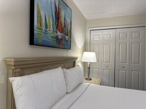 A hotel room with a bed, a painting, a nightstand, and a door. - 1402 Spacious 3/2 Resort Condo Near Disney (Orlando)
