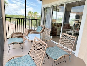 A balcony with wicker furniture, a glass table, and a view of the outdoors. - 1402 Spacious 3/2 Resort Condo Near Disney (Orlando)
