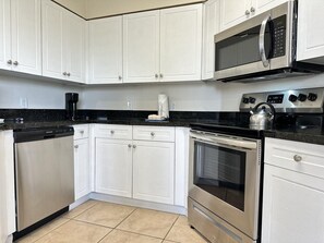 A kitchen with white cabinets, a black countertop, a stainless steel dishwasher, a microwave, a stove, and a kettle. - 1402 Spacious 3/2 Resort Condo Near Disney (Orlando)