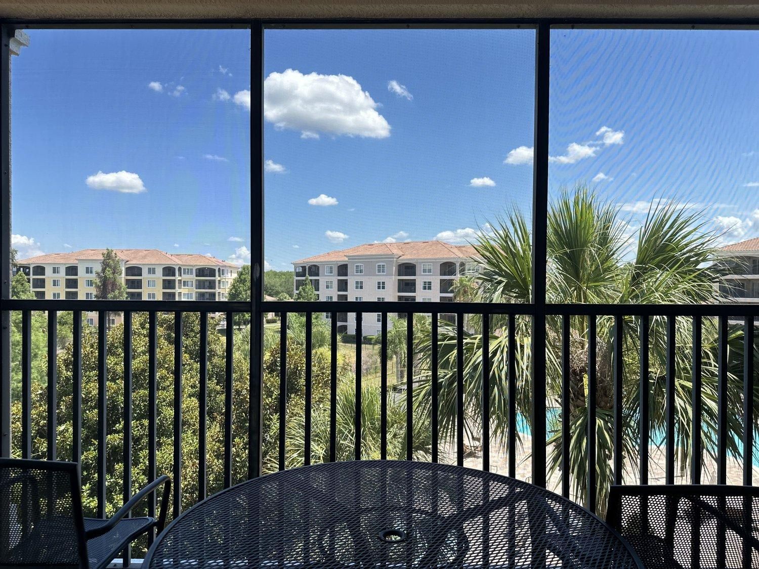 A balcony with a view of a residential area, including multi-story buildings and palm trees.