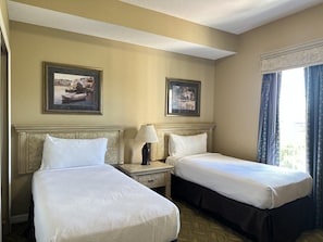 A hotel room with two beds, a nightstand with a lamp, and two framed pictures on the wall. - 1407 Spacious 3/2 Resort Condo Near Disney (Orlando)