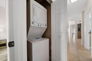 A laundry room with a washer and dryer, a door leading to a hallway, and a tiled floor.