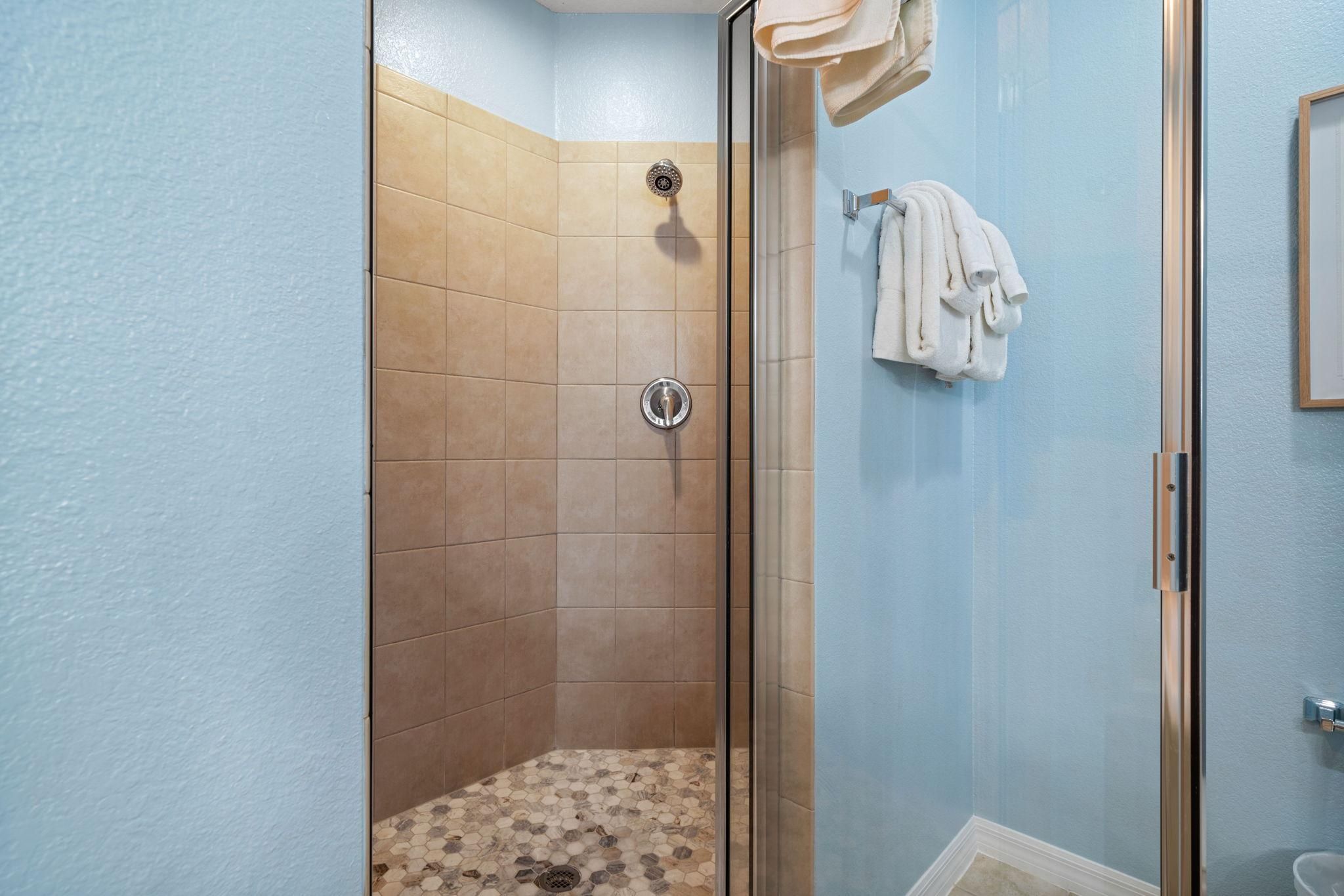 Eine Dusche mit Glastür, beigen Fliesen und einem gefliesten Boden.