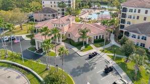 A multi-story hotel with a swimming pool, surrounded by palm trees and greenery. - 1507 Spacious 3/2 Resort Condo Near Disney (Orlando)