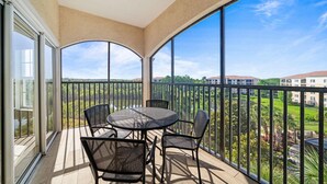 A balcony with a table and chairs, large windows, and a view of buildings and greenery. - 1507 Spacious 3/2 Resort Condo Near Disney (Orlando)