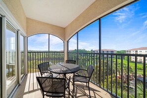 A balcony with a table and chairs, large windows, and a view of buildings and greenery.