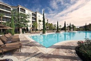 A swimming pool with lounge chairs and a building with balconies in the background.