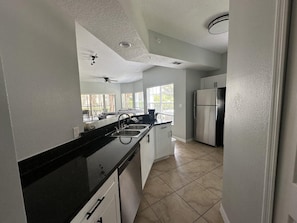 A modern kitchen with a black countertop, stainless steel appliances, and a view to the outside. - 2101 Spacious 3/2 Resort Condo Near Disney (Orlando)