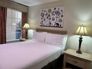 A hotel room with a bed, two bedside tables, a window with curtains, and a wall-mounted artwork. - 2102 Spacious 3/2 Resort Condo Near Disney (Orlando)