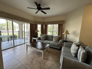 A living room with a ceiling fan, two sofas, a coffee table, and a dining area with chairs. - 2102 Spacious 3/2 Resort Condo Near Disney (Orlando)