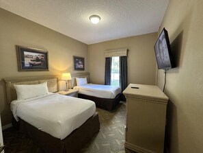 Ein Hotelzimmer mit zwei Betten, einem Schreibtisch, einem Fernseher und einem Fenster mit Vorhängen.