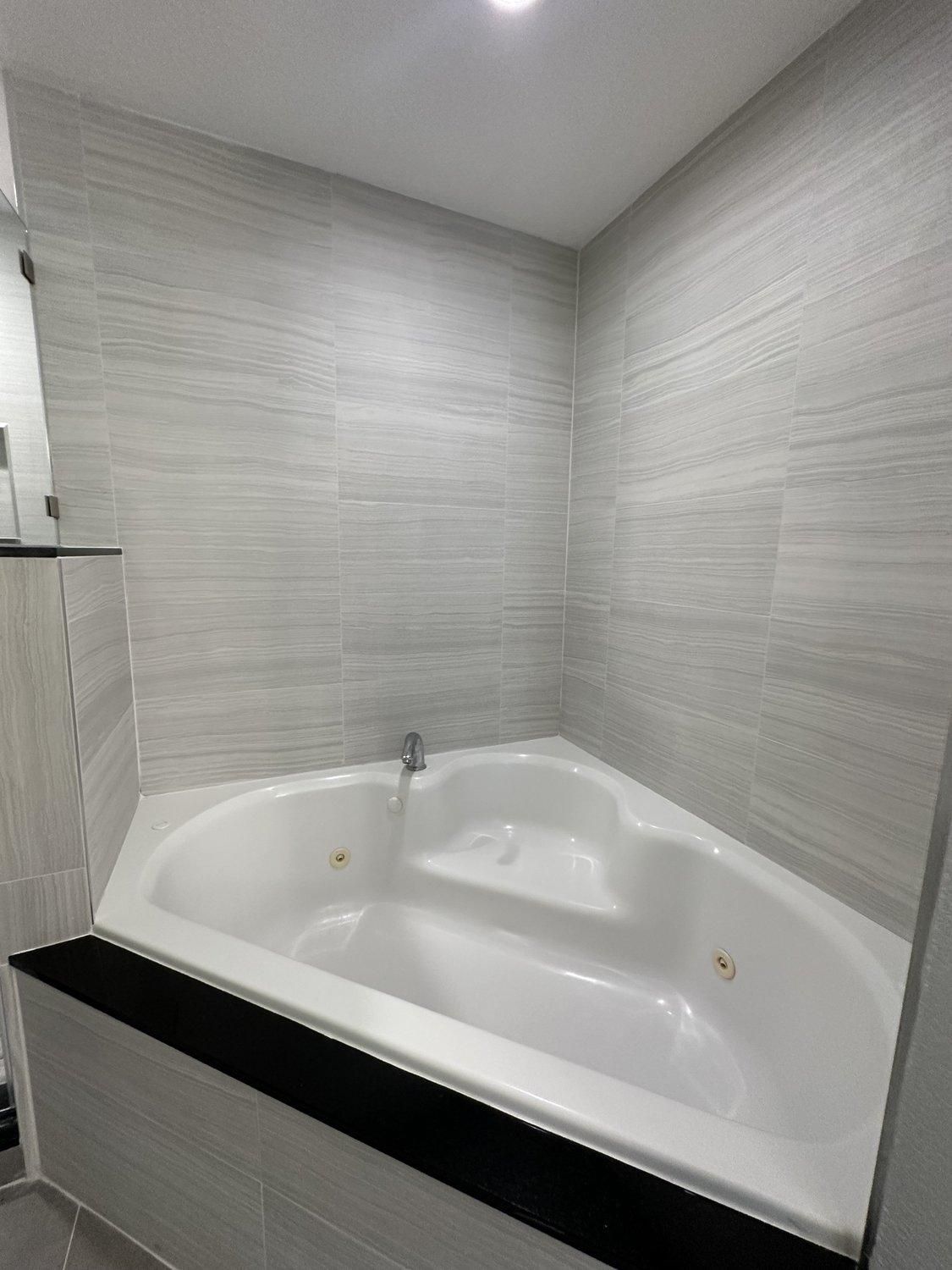 Un baño moderno con una bañera independiente, paredes con azulejos y un mostrador negro.