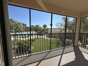 A balcony with a view of a swimming pool, palm trees, and a building in the background. - 2202 Spacious 3/2 Resort Condo Near Disney (Orlando)