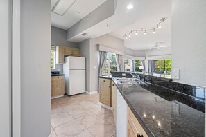 Une cuisine moderne dotée d’un îlot central, d’appareils électroménagers intégrés et offrant une vue sur l’extérieur.