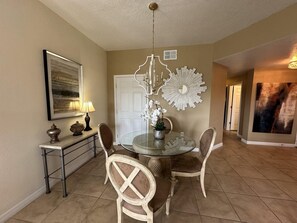 A dining area with a round glass table, two chairs, a wall-mounted light fixture, and a door in the background. - 2302 Spacious 3/2 Resort Condo Near Disney (Orlando)
