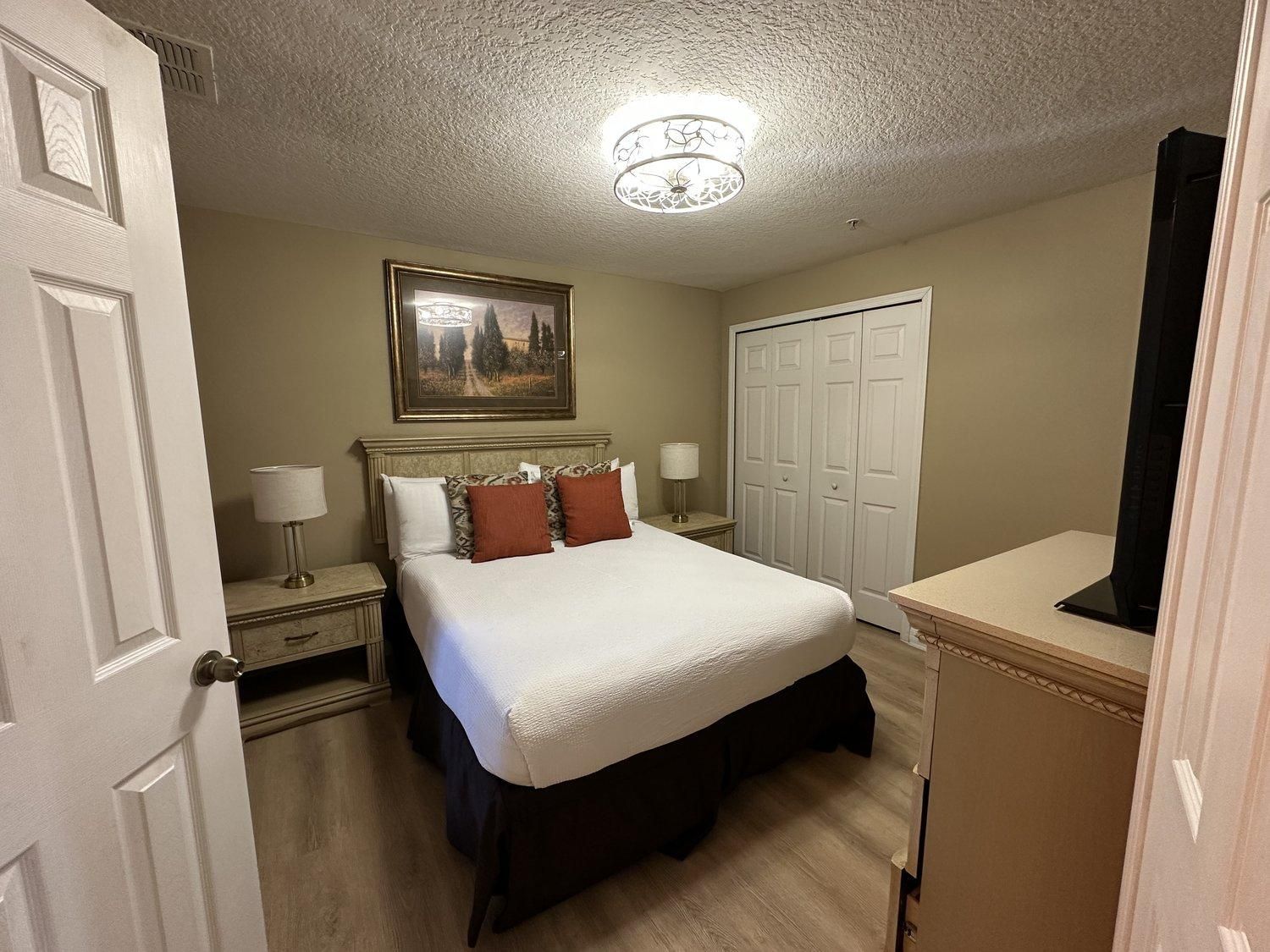 A hotel room with a bed, bedside lamps, a wardrobe, and a ceiling light fixture.