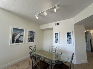 A dining area with a glass table and chairs, framed wall art, and recessed ceiling lighting. - 2402 Spacious 3/2 Resort Condo Near Disney (Orlando)