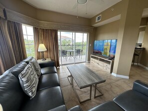 Ein Wohnzimmer mit einer Couch, einem Couchtisch, einem Fernseher und einem Balkon mit Sitzmöbeln.