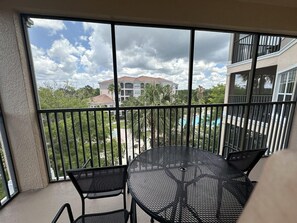 A balcony with a metal table and chairs, overlooking a swimming pool and buildings. - 2407 Spacious 3/2 Resort Condo Near Disney (Orlando)
