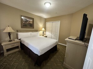 Ein Hotelzimmer mit einem Bett, zwei Nachttischen, einer Lampe, einem Fernseher, einer Tür und einem Gemälde an der Wand.