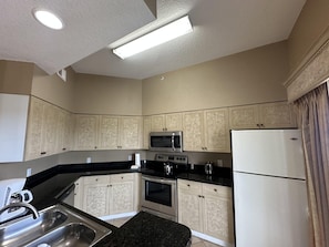 Eine kleine Küche mit weißen Schränken, einer schwarzen Arbeitsplatte, einer Edelstahlspüle, einer Mikrowelle, einem Backofen und einem Kühlschrank.
