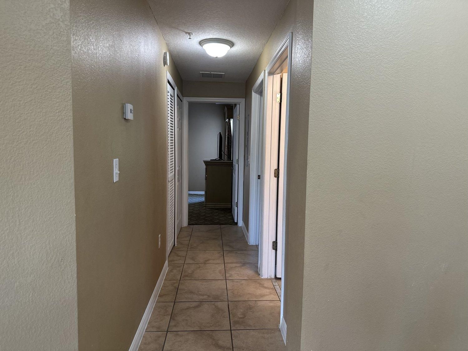 A narrow hallway with beige walls, a tiled floor, and a ceiling light.
