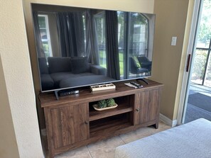 A flat-screen TV on a wooden entertainment unit with a remote control, a small plant, and a power strip. - 3102 Spacious 3/2 Resort Condo Near Disney (Orlando)