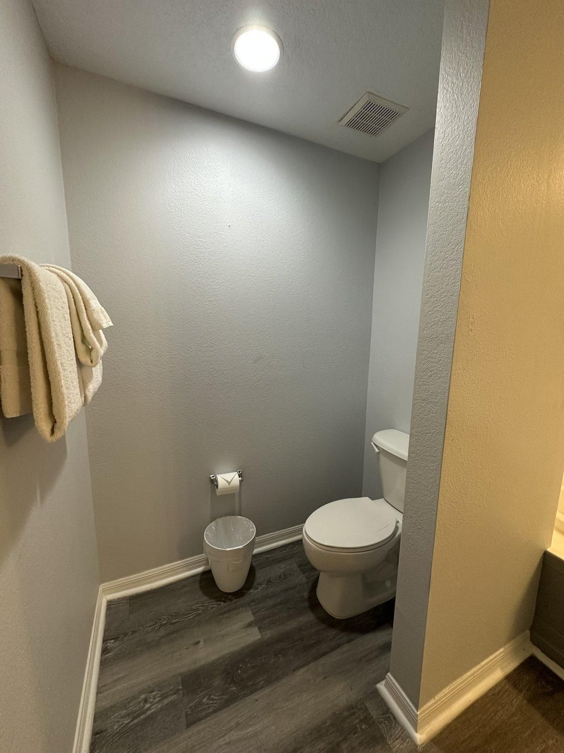 Ein Badezimmer mit Toilette, Mülleimer und einem Handtuch, das an der Wand hängt.