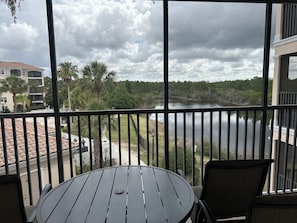 A balcony with a table and chairs, overlooking a body of water and a park with trees. - 3307 Spacious 3/2 Resort Condo Near Disney (Orlando)