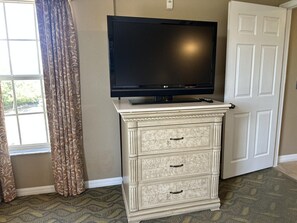 A room with a television on a cabinet, a door, and patterned curtains. - 3402 Spacious 3/2 Resort Condo Near Disney (Orlando)