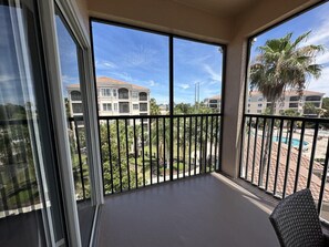 Ein Balkon mit Blick auf einen Swimmingpool, Palmen und ein mehrstöckiges Gebäude.