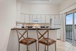 Eine moderne Küche mit weißen Schränken, einer Mikrowelle, einem Kühlschrank und einer Bar mit zwei Stühlen.