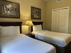 Ein Hotelzimmer mit zwei Betten, einem Nachttisch mit Lampe und zwei gerahmten Bildern an der Wand.