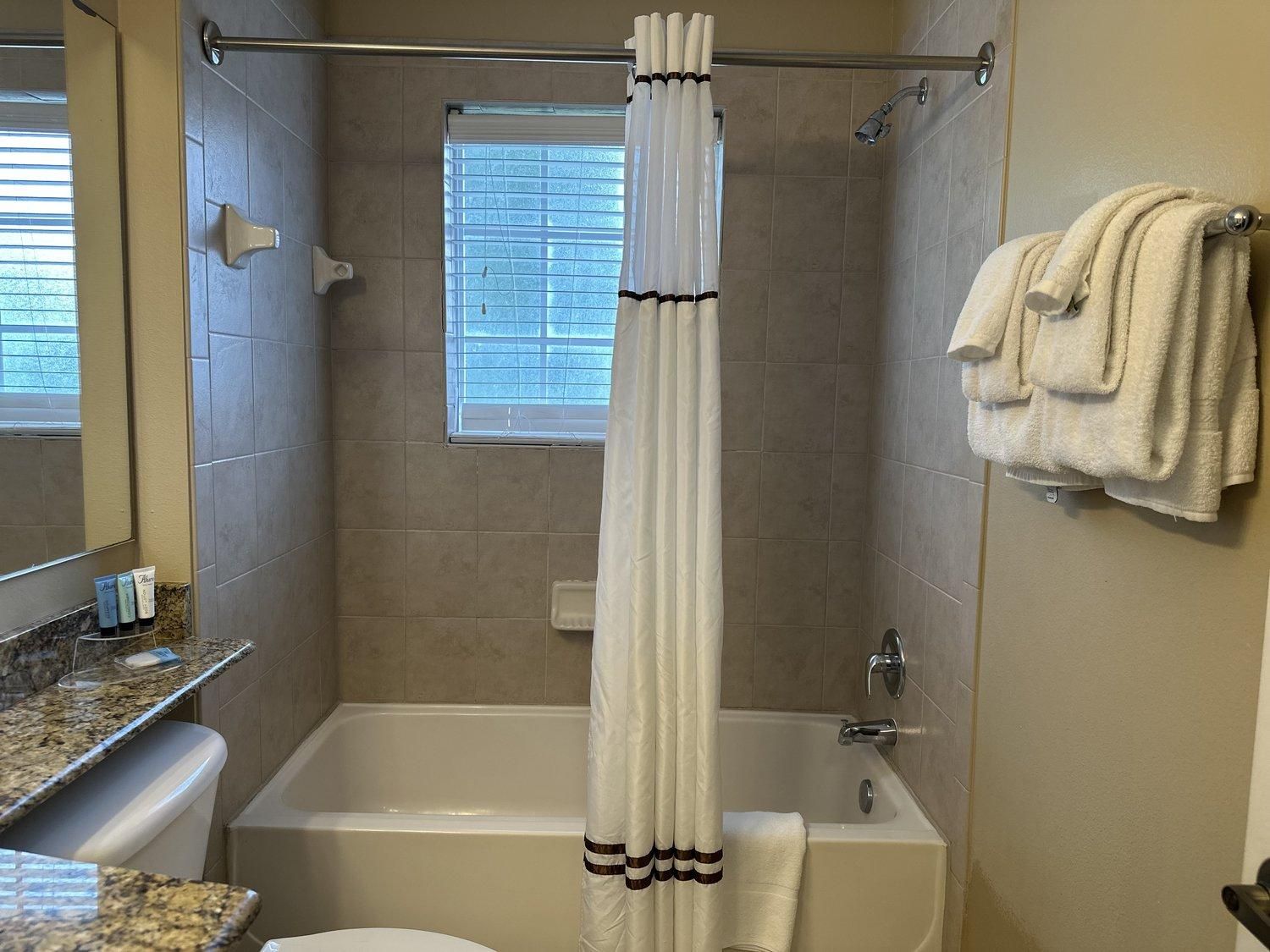 Ein Badezimmer mit einer Badewanne, einer Duschvorhang, einem Handtuchhalter und einem Fenster mit Jalousien.