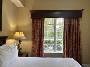 Une chambre d’hôtel avec un lit, une table de chevet avec une lampe et une fenêtre avec des rideaux.